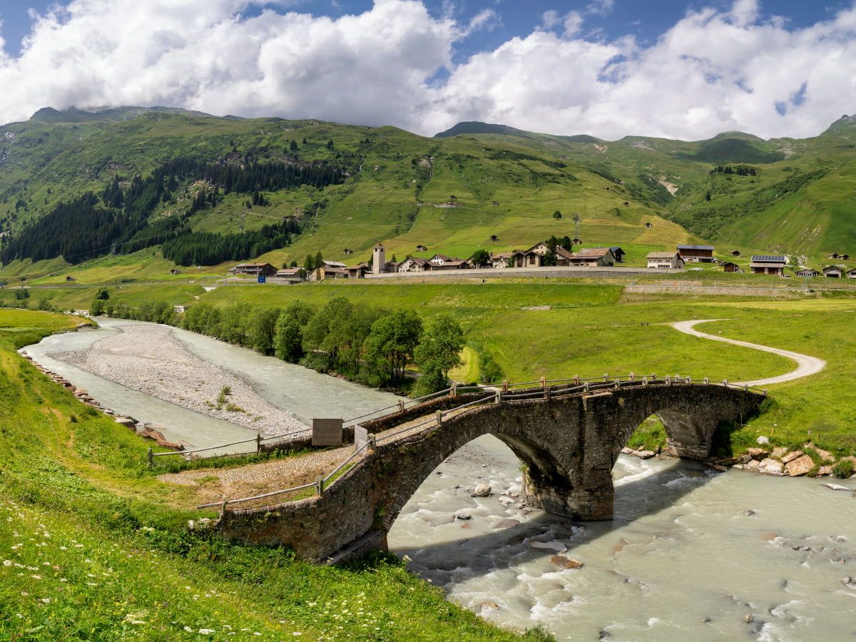 Eine historische Brücke über einen Fluss mit Schweizer Bergdorf im Hintergrund